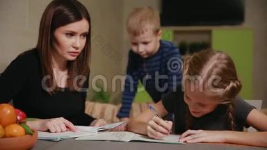 母女俩在做学校作业，一个小男孩在看。 哥哥帮忙做作业。